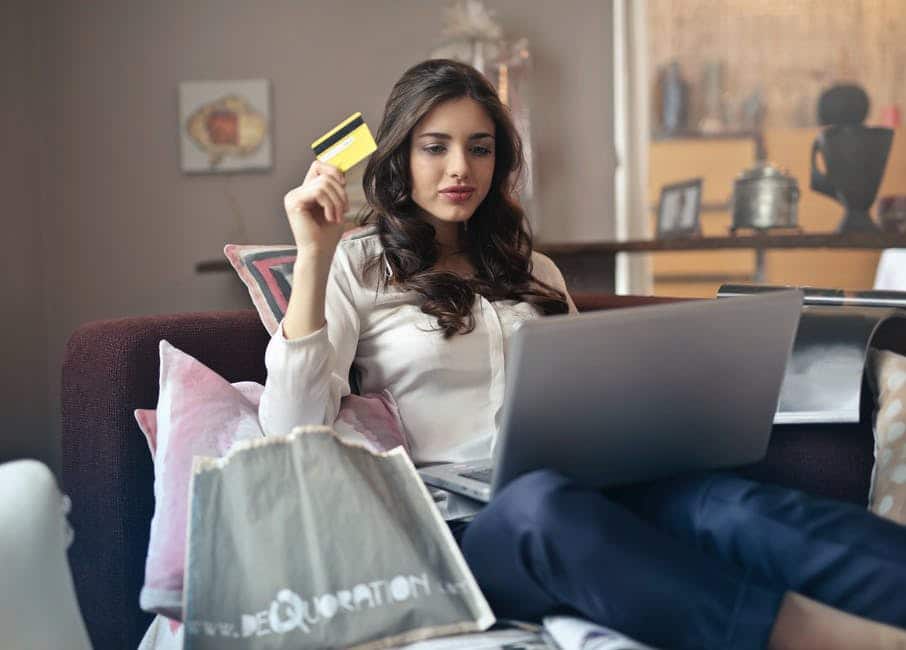 a woman sits on an armchair with a laptop and holds a credit card in her hands